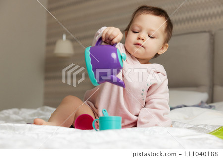 happy cute little child girl playing with tea toy cups on bed happy cute little child girl playing with tea toy cups on bed 111040188