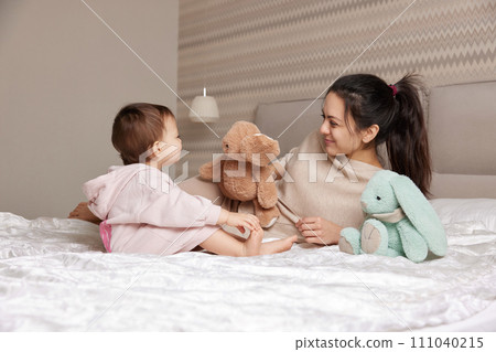 happy mother and her little child daughter playing with bunny toys in bedroom, family having fun happy mother and her little child daughter playing with bunny toys in bedroom, family having fun 111040215