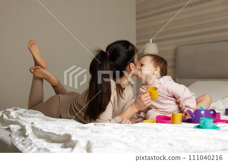 mother and little child daughter playing tea party and spending time together in bedroom, family having fun mother and little child daughter playing tea party and spending time together in bedroom, family having fun 111040216