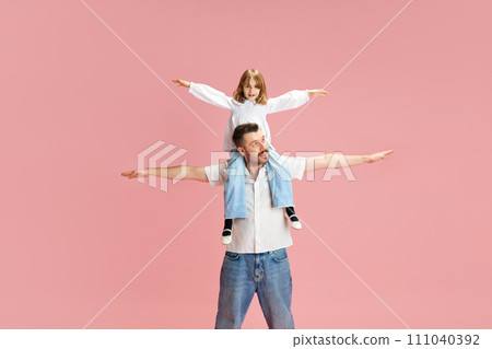 Father and daughter with arms outstretched, play airplanes pretending to fly against pink pastel background. Concept of International Day of Happiness 111040392