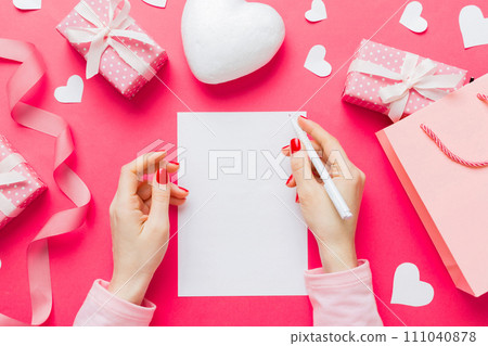 top view photo of valentine day decor female hands holding letter with envelope, small gift box and heart decoration on isolated pastel colored background with empty space 111040878