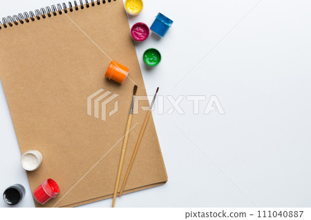 Album pages and paints, pencils, brush on a colored background. Top view with empty space. workplace for creativity. home teaching concept drawing Album pages and paints, pencils, brush on a colored background. Top view with empty space. workplace for creativity. home teaching concept drawing 111040887