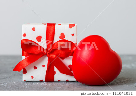 gift box with red bow and red heart on colored background. Perspective view. Flat lay gift box with red bow and red heart on colored background. Perspective view. Flat lay 111041031