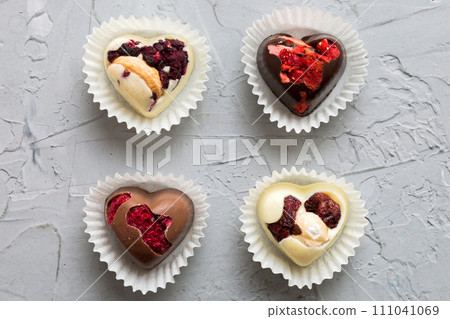 chocolate sweets in the form of a heart with fruits and nuts on a colored background. top view with space for text, holiday concept chocolate sweets in the form of a heart with fruits and nuts on a colored background. top view with space for text, holiday concept 111041069