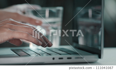 Female hands typing on computer. Business woman professional user worker typing on laptop notebook keyboard. Drink water from glass. Online work with pc software apps technologies, close up side view Female hands typing on computer. Business woman professional user worker typing on laptop notebook keyboard. Drink water from glass. Online work with pc software apps technologies, close up side view 111041087