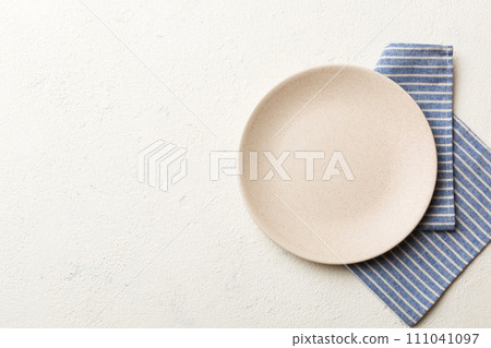 Top view on colored background empty round white plate on tablecloth for food. Empty dish on napkin with space for your design 111041097