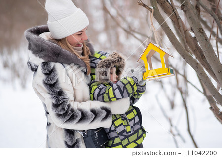 mother and son in a winter park feed birds using a feeder mother and son in a winter park feed birds using a feeder 111042200