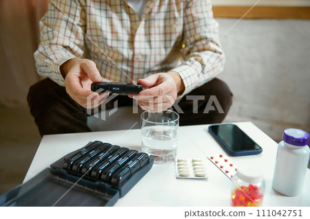 Hands of a senior man holding pill box, medication containers labeled with days of week. Organizer for daily pills and vitamins 111042751
