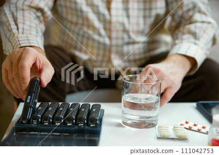 Hands of a senior man holding pill box, medication containers labeled with days of week. Organizer for daily pills and vitamins 111042753