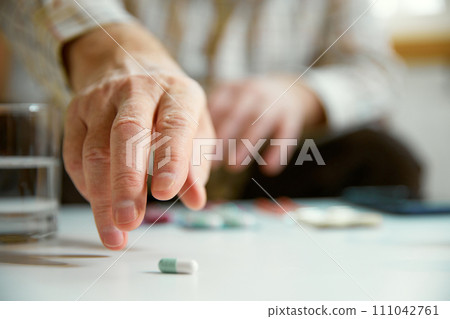 Close-up of male hands taking pills, vitamins, meds at home. Blurred background, focus on hands Close-up of male hands taking pills, vitamins, meds at home. Blurred background, focus on hands 111042761