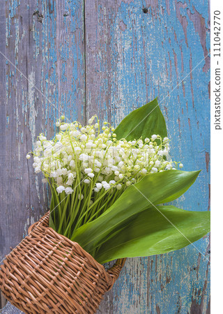 Bouquet of white lilies of the valley in a wicker basket on a blue paint old wooden background; copy space; Greeting card for international workers day 111042770