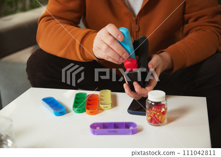 Person filling portable daily pill organizer from pill container, with other pill compartments 111042811