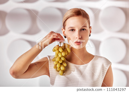 Portrait of a blonde girl holding a bunch of grapes, beauty concept. Portrait of a blonde girl holding a bunch of grapes, beauty concept. 111043297