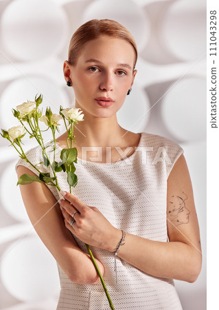 Portrait of a beautiful young disabled woman, born without an arm, holding a flower in her hands in a white dress. Diversity disability and flowers. Portrait of a beautiful young disabled woman, born without an arm, holding a flower in her hands in a white dress. Diversity disability and flowers. 111043298