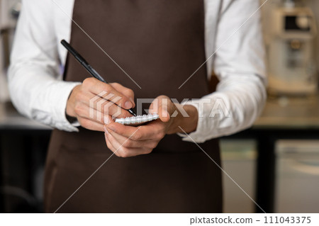 Pizzeria worker in apron making notes for order preparation Pizzeria worker in apron making notes for order preparation 111043375
