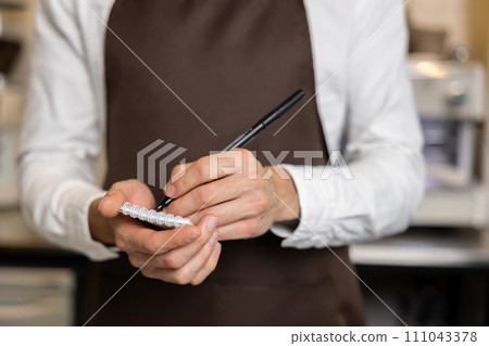 Pizzeria worker in apron making notes for order preparation Pizzeria worker in apron making notes for order preparation 111043378