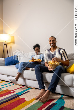 Man and woman enjoying leisure time together eating pizza and popcorn while sitting on couch Man and woman enjoying leisure time together eating pizza and popcorn while sitting on couch 111043402