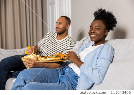 Couple eating pizza and popcorn watching comedy film sitting on couch indoor 111043406