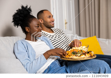 Man and woman family enjoying movie on weekend eating pizza and popcorn while sitting on couch Man and woman family enjoying movie on weekend eating pizza and popcorn while sitting on couch 111043409