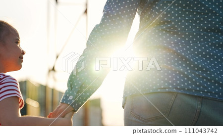Cute baby girl jumping rejoice positive emotion holding mother hand outdoor bright sun light closeup 111043742