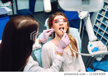 Young woman at the dentist's chair during a dental procedure. Overview of dental caries prevention. Young woman at the dentist's chair during a dental procedure. Overview of dental caries prevention. 111043846