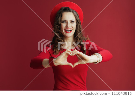 smiling elegant female in dress and beret showing heart hands 111043915