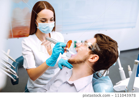 Young man at the dentist's chair during a dental procedure. Overview of dental caries prevention. 111043978