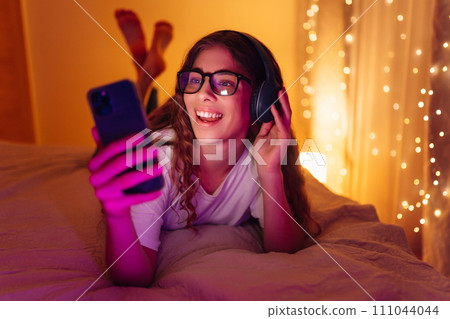 Woman communicates with friends on smartphone in headphones while sitting at home. Freelance concept Woman communicates with friends on smartphone in headphones while sitting at home. Freelance concept 111044044