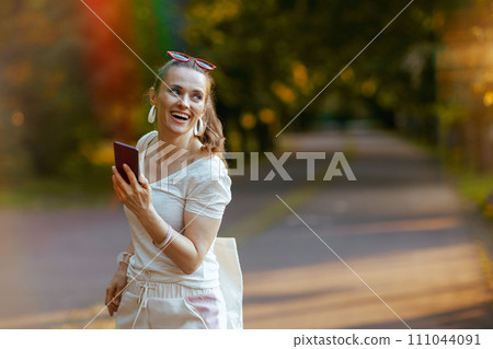 smiling stylish woman in white shirt with smartphone walking smiling stylish woman in white shirt with smartphone walking 111044091