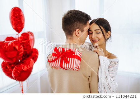 Young couple at home celebrating Valentine's Day. Exchange of gifts. Surprise and love concept. 111044221