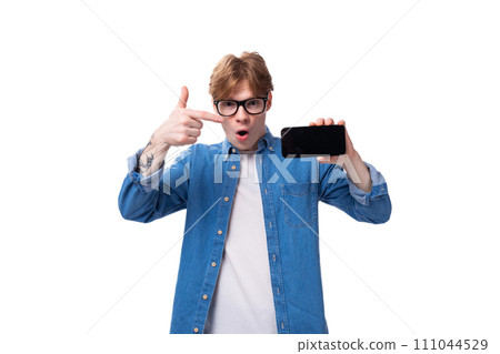 a young red-haired guy dressed in a blue shirt shows an advertisement on a smartphone 111044529