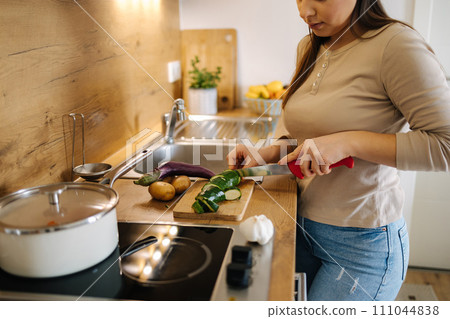Beautiful young female cutting vegetables on kitchen at home. Home food concept Beautiful young female cutting vegetables on kitchen at home. Home food concept 111044838