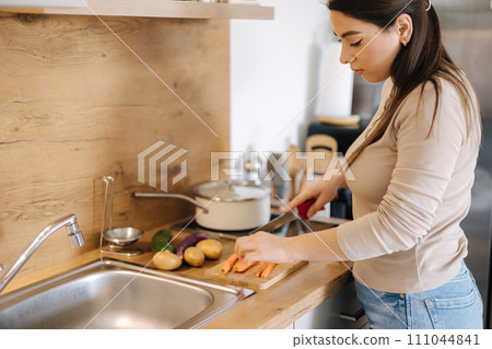 Female using knife and cutting carrot on wooden table. Home food concept  111044841