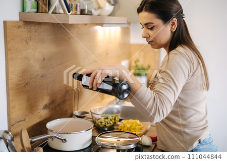 Beautiful woman adds olive oil into saucepan and cooking vegan Mexican food. 111044844