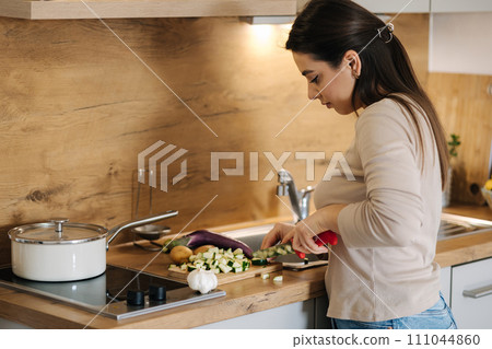 Beautiful young female cutting vegetables on kitchen at home. Home food concept 111044860