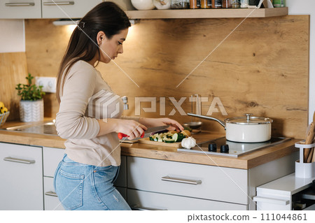 Beautiful young female cutting vegetables on kitchen at home. Home food concept Beautiful young female cutting vegetables on kitchen at home. Home food concept 111044861