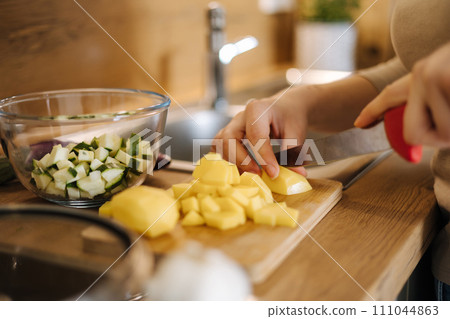 Close-up of female cutting potato on wooden board at home. Home made food concept Close-up of female cutting potato on wooden board at home. Home made food concept 111044863
