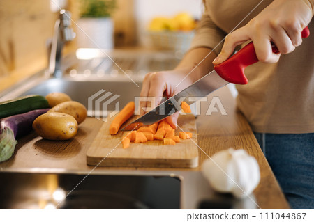 Close-up of female using knife and cutting carrot on wooden table. Home food concept  111044867