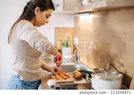 Female using knife and cutting carrot on wooden table. Home food concept  111044871