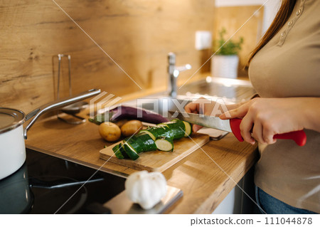 Side view of woman cutting zucchini on a wooden board. Home food concept Side view of woman cutting zucchini on a wooden board. Home food concept 111044878
