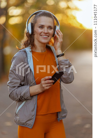 happy fit woman in fitness clothes in park with headphones 111045177