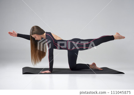 Beautiful Caucasian female practicing bird dog yoga pose on mat. Side view of calm sporty woman in black activewear performing Parsva Balasana, isolated on grey studio background. Yoga concept. 111045875