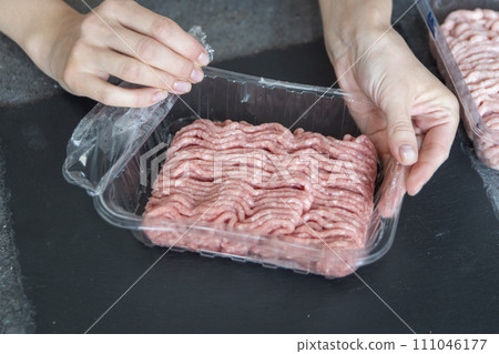 A hand opens a pack of fresh minced meat close-up. The process of cooking tasty cutlets. 111046177
