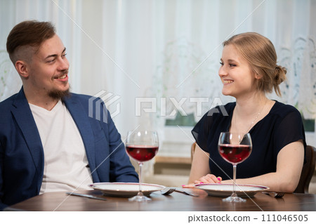 A girl and a boy talk over a glass of wine. 111046505