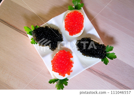 Halves of a hard-boiled chicken egg with red caviar on a wooden background. Put black caviar on an egg to serve delicious healthy food High quality Halves of a hard-boiled chicken egg with red caviar on a wooden background. Put black caviar on an egg to serve delicious healthy food High quality 111046557