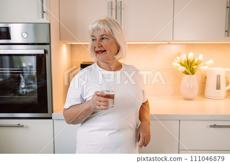 Senior 60s woman drinking pure water from glass in kitchen. Space for text Senior 60s woman drinking pure water from glass in kitchen. Space for text 111046879