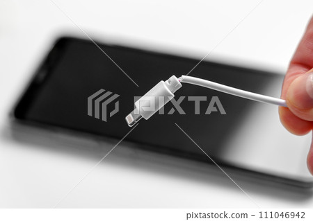 Broken charger cable in hand with smartphone close up. Faulty electronics concept 111046942