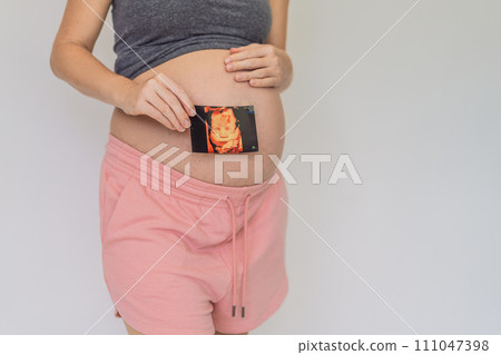 Expectant mother tenderly connects with her unborn child, holding ultrasound photo to her pregnant belly 111047398