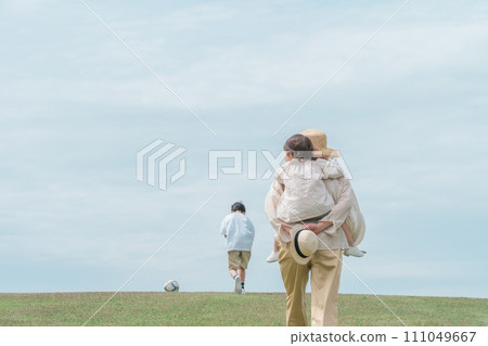 A mother carrying her daughter on her back on the lawn in a park with blue skies, mother and daughter, parent and child, girl, boy, soccer ball A mother carrying her daughter on her back on the lawn in a park with blue skies, mother and daughter, parent and child, girl, boy, soccer ball 111049667