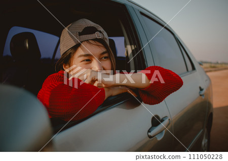 Young Asian woman leaning out of car window looking out to the field. Young Asian woman leaning out of car window looking out to the field. 111050228